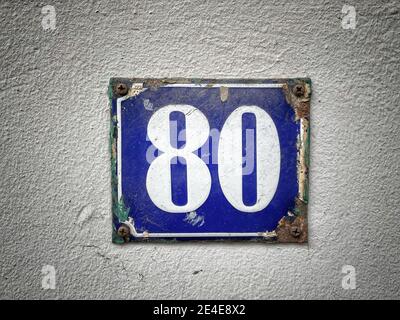 Numero 80, il numero di case, appartamenti, strade. Il numero bianco su una piastra di metallo blu, ospita il numero ottanta (80) su una parete ruvida. Foto Stock