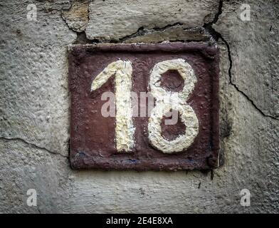 Numero 18, il numero di case, appartamenti, strade. Il numero bianco su una piastra di metallo marrone, ospita il numero diciotto (18) su una parete ruvida. Foto Stock