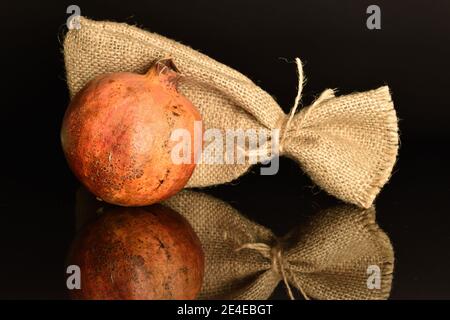 Un melograno intero, rosso scuro maturo, succosa e dolce, con una borsa di iuta, su sfondo nero. Foto Stock