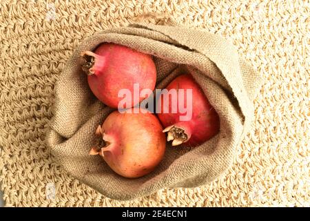 Tre melograni maturi organici in un sacchetto di iuta, primo piano, su un tappetino di paglia. Foto Stock