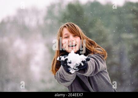 Una ragazza con un sorriso sincero tiene fuori un globo di neve alla macchina fotografica. Foto sullo sfondo di una foresta innevata invernale. Foto Stock