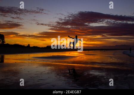 Silhouette di un giovane uomo salto sulla spiaggia di nelson durante il tramonto sulla Spiaggia Tahunanui di Nelson, Nuova Zelanda. Foto Stock