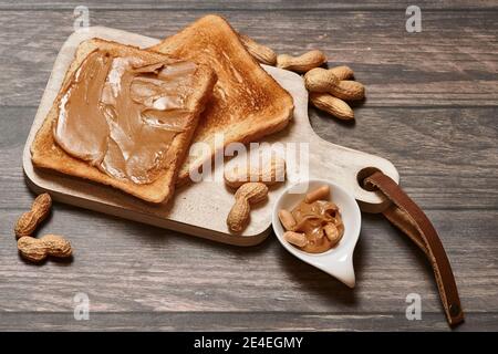 Prima colazione con burro di arachidi cremoso toast su un tavolo da cucina in legno con arachidi fresche. Foto Stock