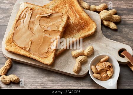 Colazione dolce con pane tostato al burro di arachidi su una cucina in legno tavola con arachidi fresche Foto Stock