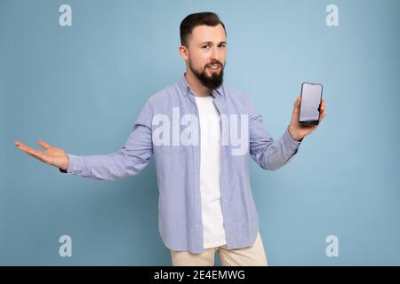 Foto di un bel bel bel bell'uomo giovane brunetta che non si rasa con barba che indossa una t-shirt bianca casual e una maglietta blu isolato su blu Foto Stock