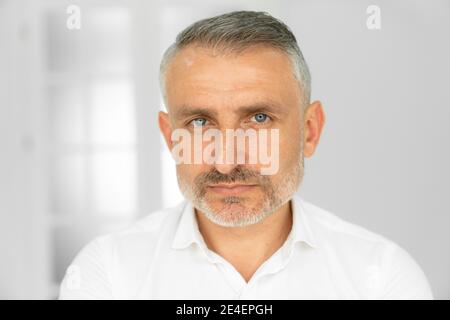 Uomo medio-anziano bearded che guarda la macchina fotografica con un'espressione seria in un ritratto di testa e spalle ravvicinato Foto Stock
