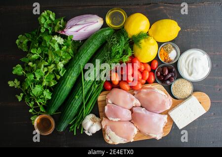 Mediterranean Chicken Bowl pasto ingredienti: Cosce di pollo disossate senza pelle con frutta, verdure, erbe e spezie su uno sfondo di legno scuro Foto Stock