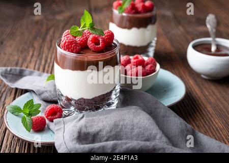 Delizioso dessert a strati con formaggio cremoso, biscotti al cioccolato schiacciati, condito con ganache e lamponi freschi in un vasetto Foto Stock
