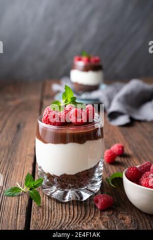 Delizioso dessert a strati con formaggio cremoso, biscotti al cioccolato schiacciati, condito con ganache e lamponi freschi in un vasetto Foto Stock