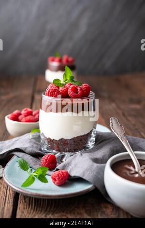Delizioso dessert a strati con formaggio cremoso, biscotti al cioccolato schiacciati, condito con ganache e lamponi freschi in un vasetto Foto Stock