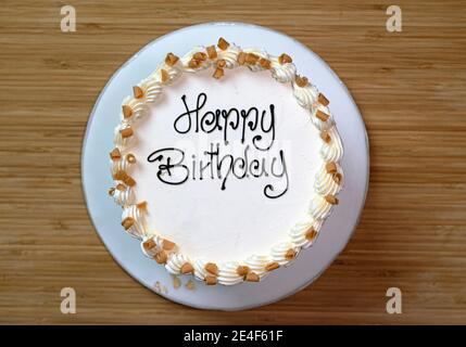 Torta di compleanno gourmet bianca con un cartello 'buon compleanno', smerigliata con crema di burro e decorata con scaglie di caramello Foto Stock