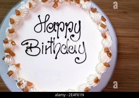 Torta di compleanno gourmet bianca con un cartello 'buon compleanno', smerigliata con crema di burro e decorata con scaglie di caramello Foto Stock