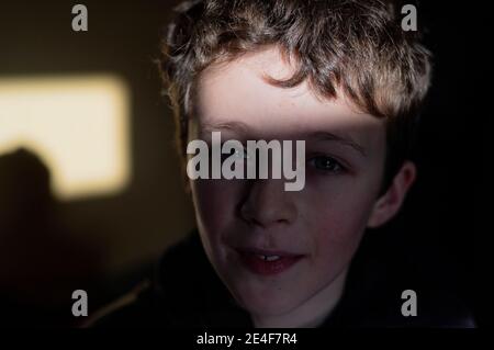 Un ritratto di un ragazzo di nove anni. Mezzo in ombra con un albero di luce solare. Foto Stock