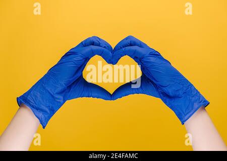 Primo piano delle mani maschili in guanti blu di protezione medica rendere il simbolo del cuore come un modo per mostrare gratitudine a medici e infermieri per aiuto Foto Stock