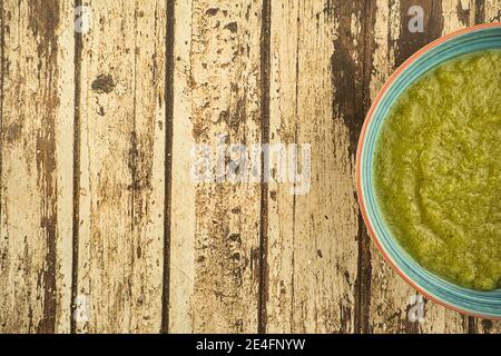 un piatto blu di zuppa di crema verde vegetale fresco servita su sfondo rustico, cibo Foto Stock