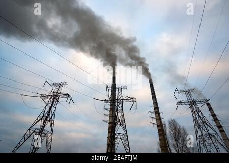 Linee elettriche ad alta tensione e tubi per centrali a carbone con fumo nero che si muovono verso l'alto in atmosfera inquinante. Foto Stock