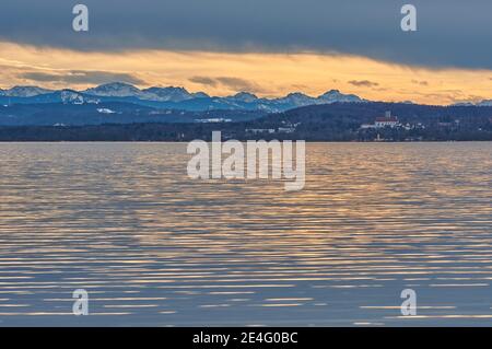 Lago riflettente durante il tramonto con una catena montuosa sullo sfondo. Lago Ammersee in Baviera, Germania al tramonto. Foto Stock