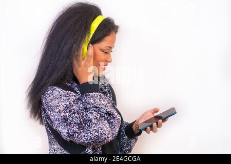 Ritratto di una donna ispanica sorridente su cuffie con un telefono e scelta di un brano da riprodurre Foto Stock