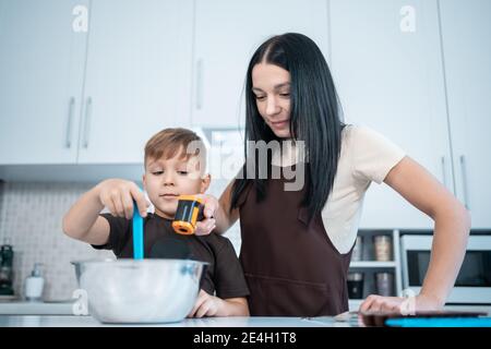 madre e capretto fanno i dolci domestici e misurano il cioccolato fuso cucina moderna Foto Stock