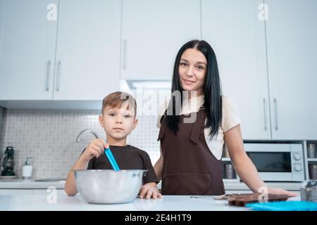 madre e capretto fanno i dolci domestici e misurano il cioccolato fuso cucina moderna Foto Stock