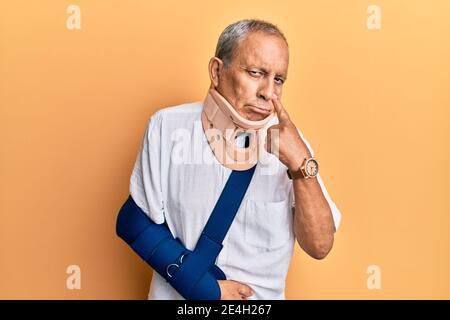 Bell'uomo anziano maturo che indossa collo cervicale e braccio su imbracatura che punta all'occhio che ti guarda gesto, espressione sospetta Foto Stock