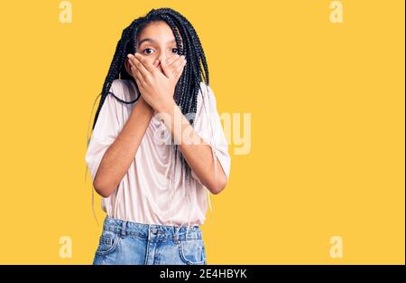Carino african american ragazza indossando abiti casual scioccato coprendo la bocca con le mani per errore. Concetto segreto. Foto Stock