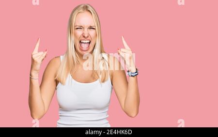 Ragazza giovane bionda che indossa stile casual con camicia senza maniche gridando con espressione pazza facendo simbolo rock con le mani in su. Stella di musica. Musica pesante c Foto Stock