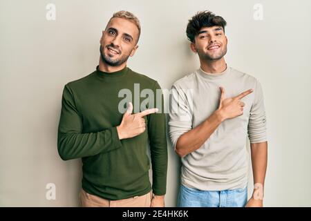 Coppia omosessuale gay in piedi insieme indossando abiti casual sorridente allegro puntare con la mano e il dito verso l'alto Foto Stock