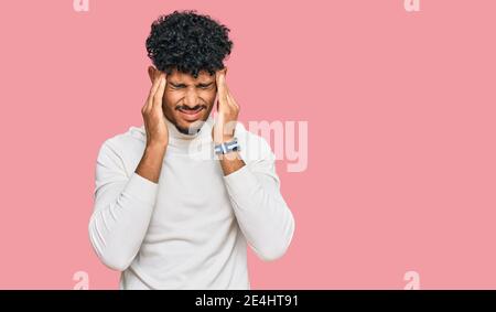 Giovane arabo che indossa un maglione invernale casual con la mano sulla testa, mal di testa perché stress. Che soffre di emicrania. Foto Stock