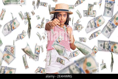 Giovane afroamericana con trecce che indossano cappello estivo pugno di pugno per combattere, aggressivo e arrabbiato attacco, minaccia e violenza Foto Stock