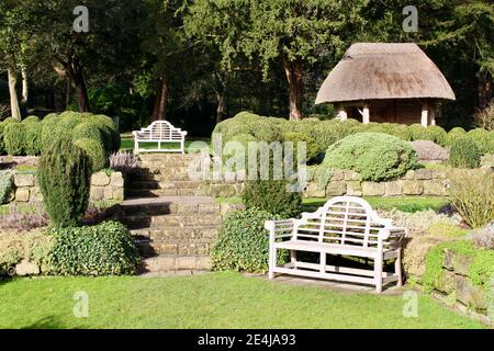 Giardino sommerso nei giardini del West Dean con posti a sedere e casa estiva rustica con tetto in paglia. West Dean, Chichester, West Sussex. Foto Stock