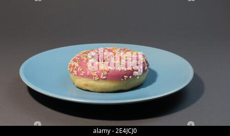 Ciambella o ciambella rosa dolce con spruzzette colorate su sfondo blu. Ammorso il sacchetto americano. Foto Stock