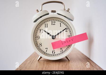Concetto di procrastinazione e ritardo. Nota appiccicosa con parola più tardi sulla sveglia bianca. Tempo di urgenza Foto Stock