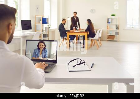 Lavoratore in ufficio che effettua una videochiamata su un computer portatile e parla con un collega, un cliente o un allenatore online Foto Stock