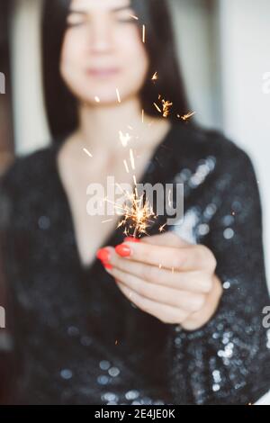 Donna che indossa un abito scintillante che tiene in mano lo scintillatore mentre si trova a casa Foto Stock