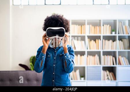 Donna che usa la cuffia per realtà virtuale mentre si sta a casa Foto Stock