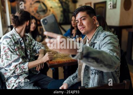 Giovane uomo che prende selfie con gli amici tramite il telefono cellulare a. ristorante Foto Stock