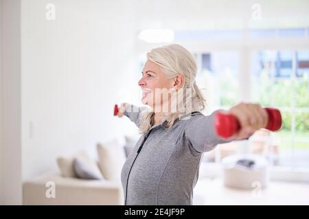 Donna anziana sorridente che si esercita con manubri a casa Foto Stock