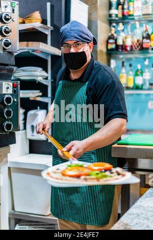 Ritratto di chef maschile indossando maschera protettiva che tiene la buccia con pizza appena fatta Foto Stock