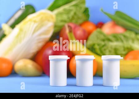 Integratori alimentari bottiglie di supplemento di fronte a frutta e verdura su sfondo sfocato Foto Stock