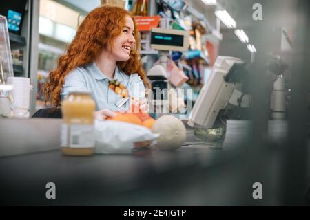 Donna di lavoro in un supermercato che lavora al banco del check-out. Donna cassiere che scannerizzare gli articoli della drogheria per il cliente. Foto Stock