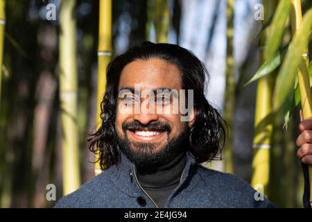 Primo piano di un giovane sorridente bearded che guarda via contro il bambù alberi Foto Stock