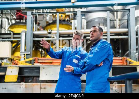 I tecnici maschi sicuri in cappotto blu discutono mentre si levano in piedi dentro industria Foto Stock