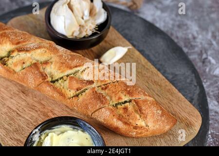 Pane Baguette fresco al forno e farcito con burro di erbe tagliere di legno Foto Stock
