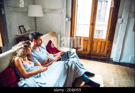 Giovane coppia seduto sul divano a casa guardando il computer portatile Foto Stock