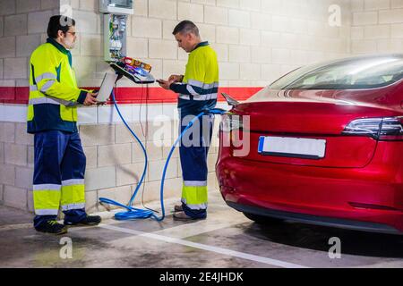 I programmatori maschi discutono mentre caricano l'automobile elettrica nella riparazione automatica negozio Foto Stock