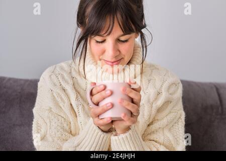 Donna che ha il caffè in tazza mentre a casa durante l'inverno Foto Stock