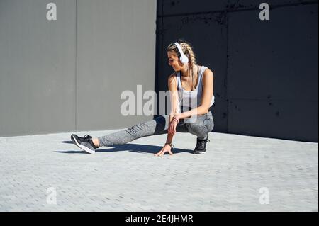 I giovani atleti indossano cuffie che si allungano mentre si accovacciano sul sentiero Foto Stock