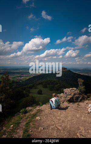 esploratrice femminile ammirando la vista del Castello di Burg Hohenzollern mentre si siede sulla montagna all'Alb Svevo, Germania Foto Stock