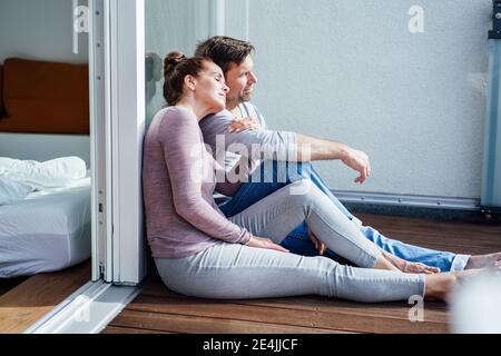 Coppia matura seduta in balcone mentre si appoggia sul vetro durante giorno di sole Foto Stock